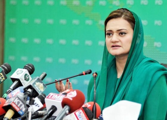 Marriyum Aurangzeb, a prominent Pakistani politician, speaking confidently at a press conference, with microphones and reporters in front of her