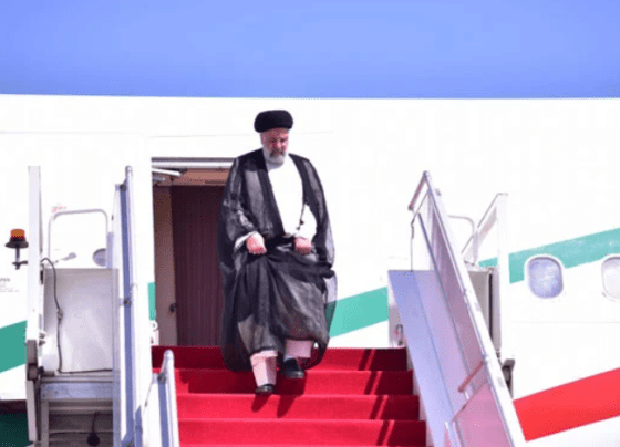 Ebrahim Raisi stepping off the airplane, greeted by Pakistani officials on the tarmac, with flags of Iran and Pakistan on display.